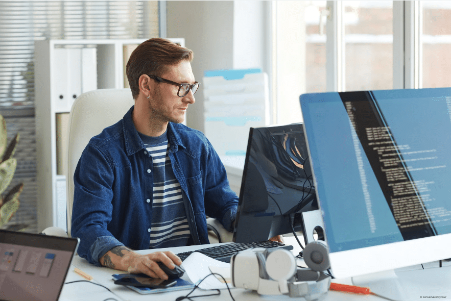 Ein Mann sitzt an einem Tisch und schaut auf einen Monitor.